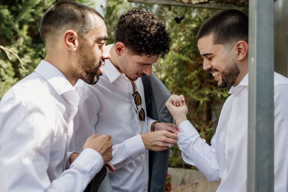 Three people in white dress shirts gather closely together sharing a lighthearted moment during an outdoor event.