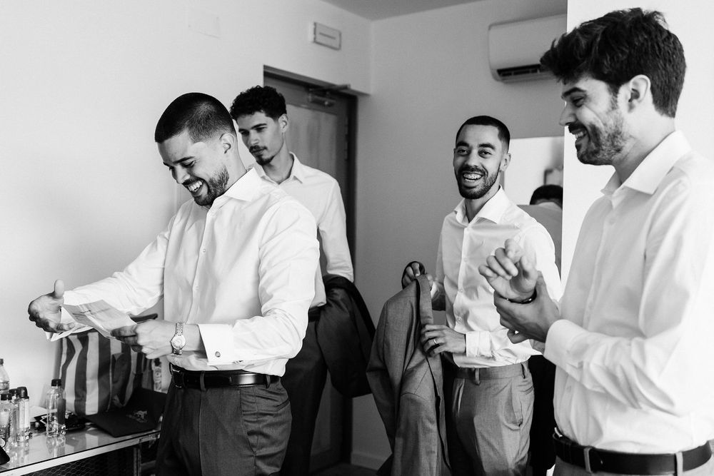 Professional colleagues in white shirts stand talking and laughing together in an office setting.