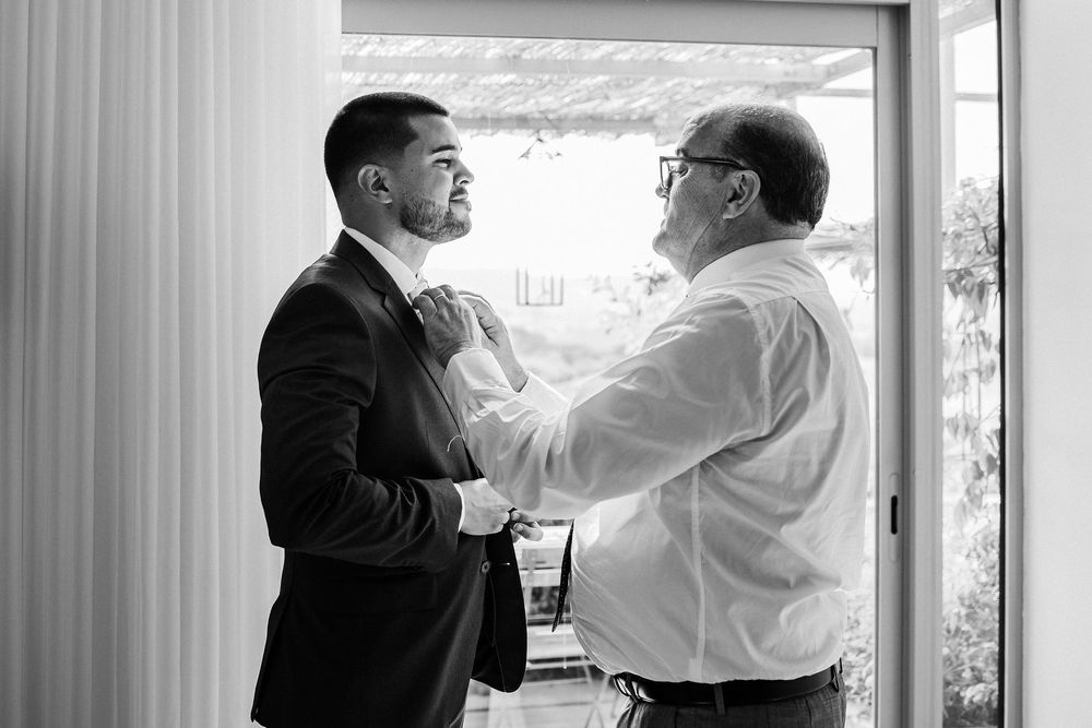A tender black and white moment between two men adjusting formal attire before a special event.