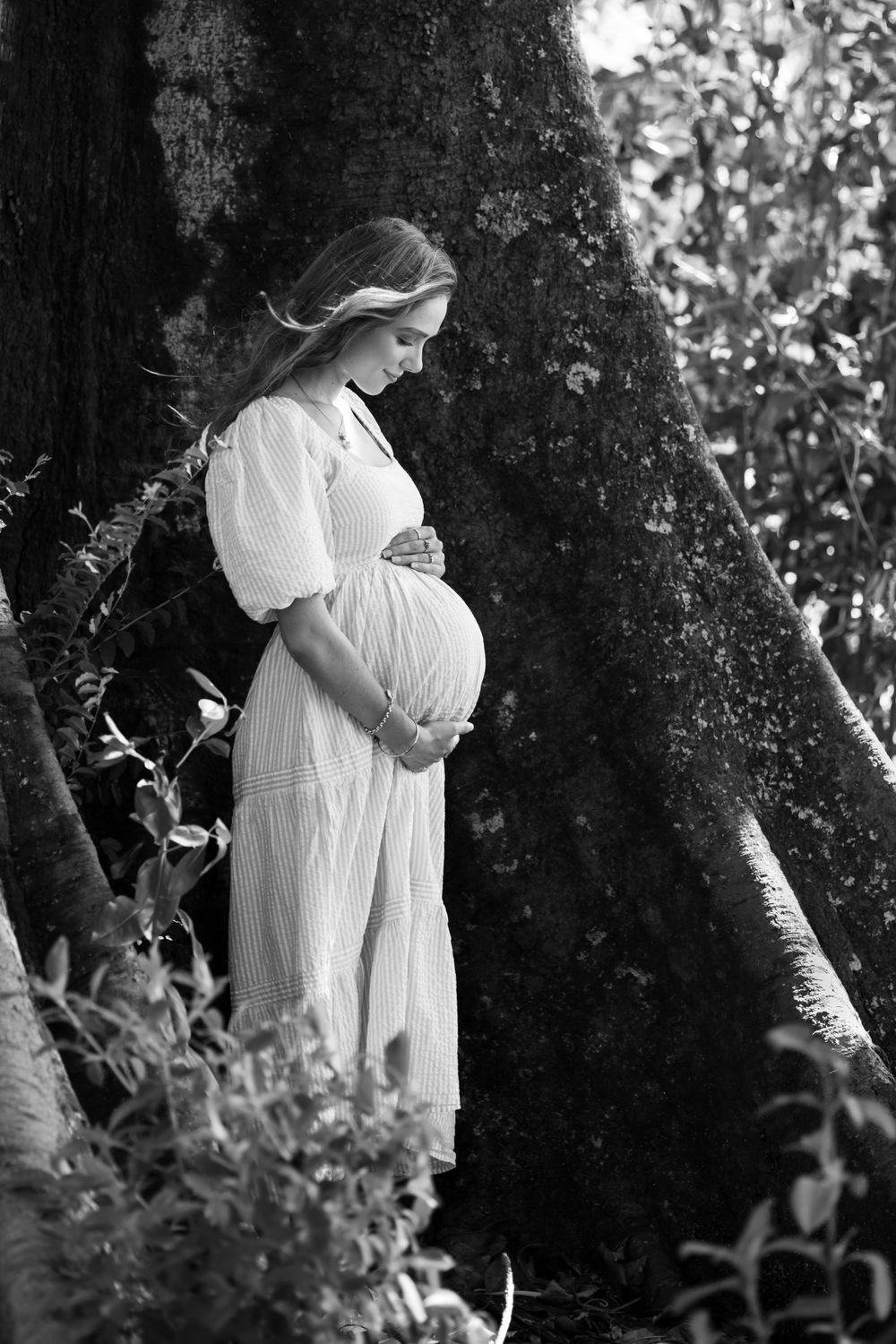 Profile view of pregnant mother embracing her belly amongst trees. Black and white.