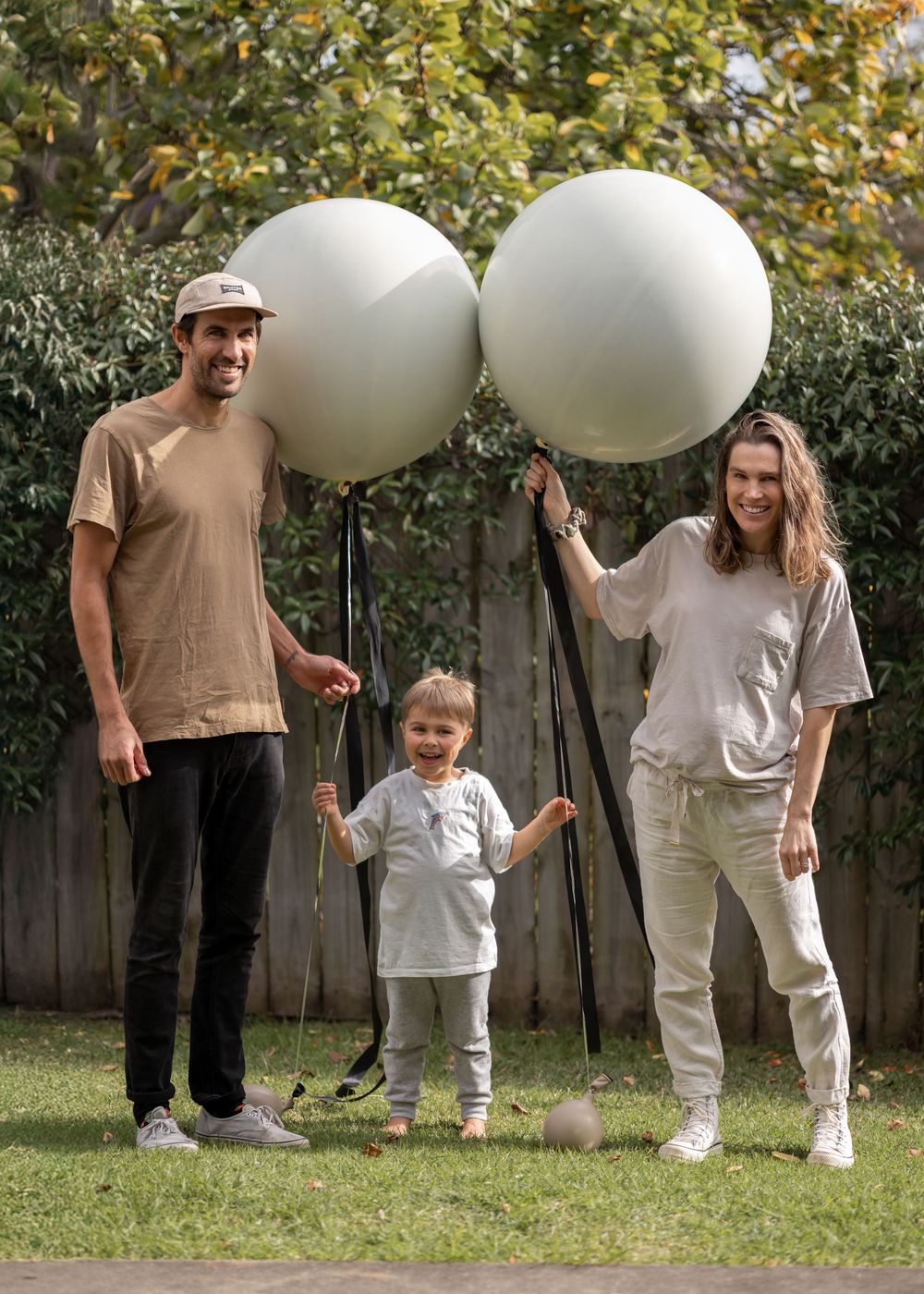 Family stand with huge balloons and pose for a photo before popping the balloons for a twin gender reveal. Boy and girl. Family photoshoot