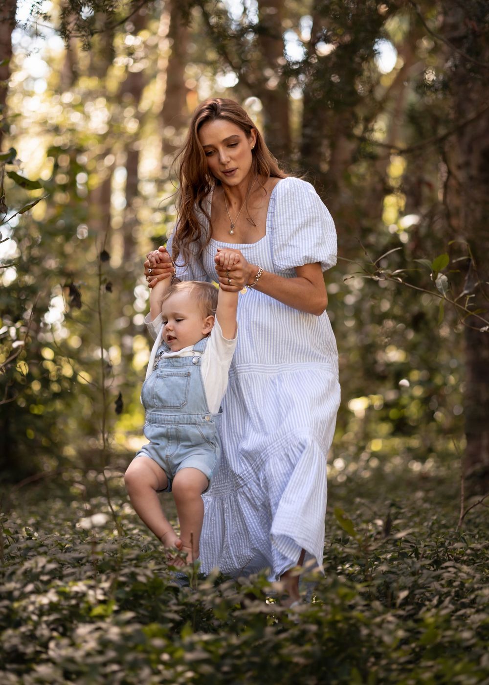 Heavily pregnant mother lifts her toddler up by the hands whilst walking through the scrub deep in the forest