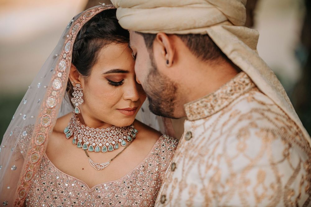 A romantic wedding scene with two elegantly dressed people in traditional Indian attire sharing an intimate moment.