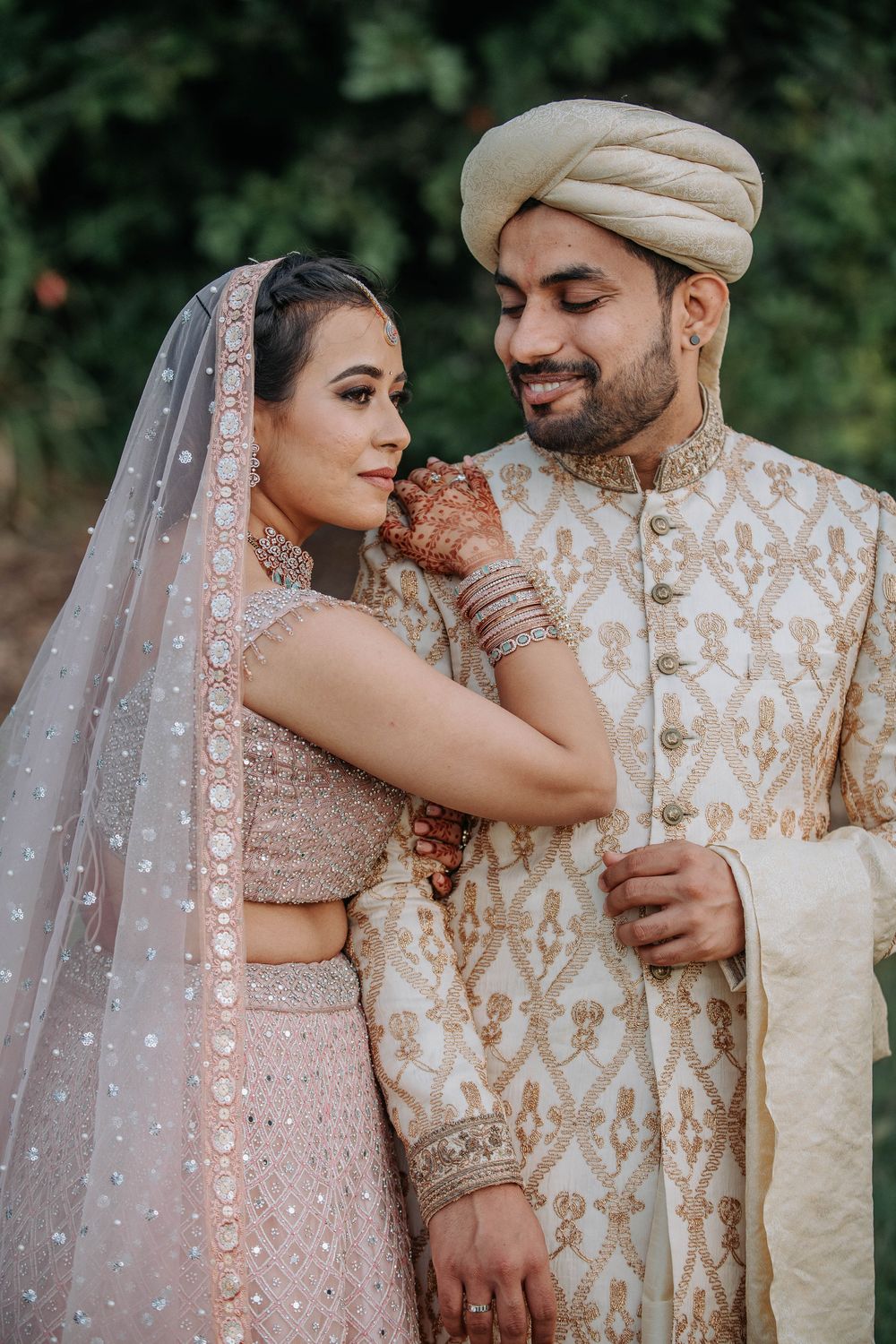A couple in traditional South Asian wedding attire embraces outdoors in a romantic photo series.