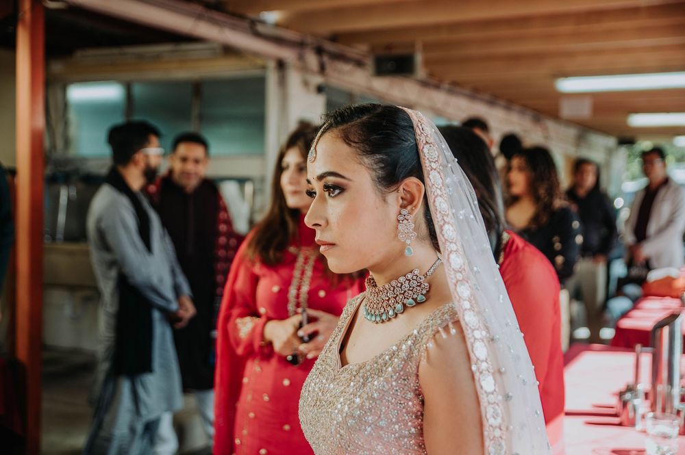 A bride in an elegant white dress with shimmering details and veil stands among guests at an indoor venue.