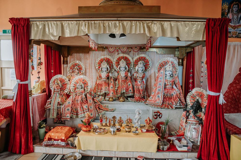Hindu temple altar decorated with red curtains, ornate deities, and traditional ceremonial offerings on display.