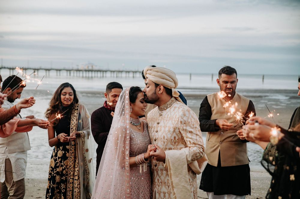 A romantic beach wedding ceremony with guests celebrating by a pier during golden hour on the coast.