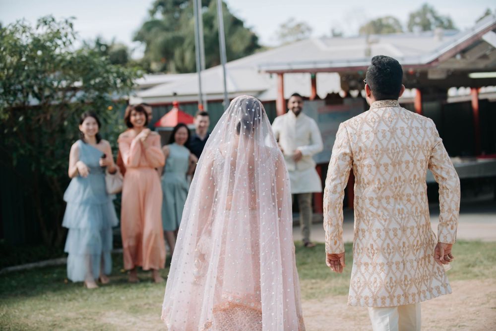 Wedding guests in traditional South Asian attire gather outdoors during a celebration with peach and pink colors.