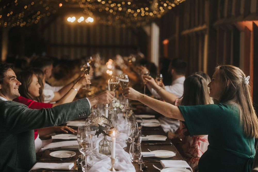 Elegant dinner party setting with string lights and wine glasses on a rustic wooden table in warm lighting.