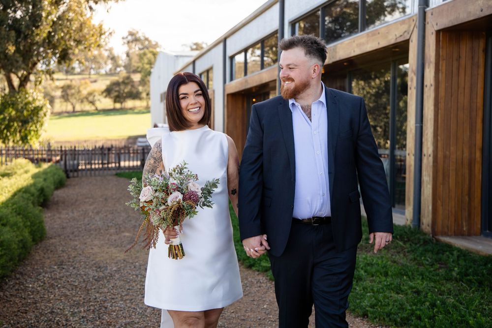 A couple walks along a rustic path holding hands on their wedding day at a countryside venue.