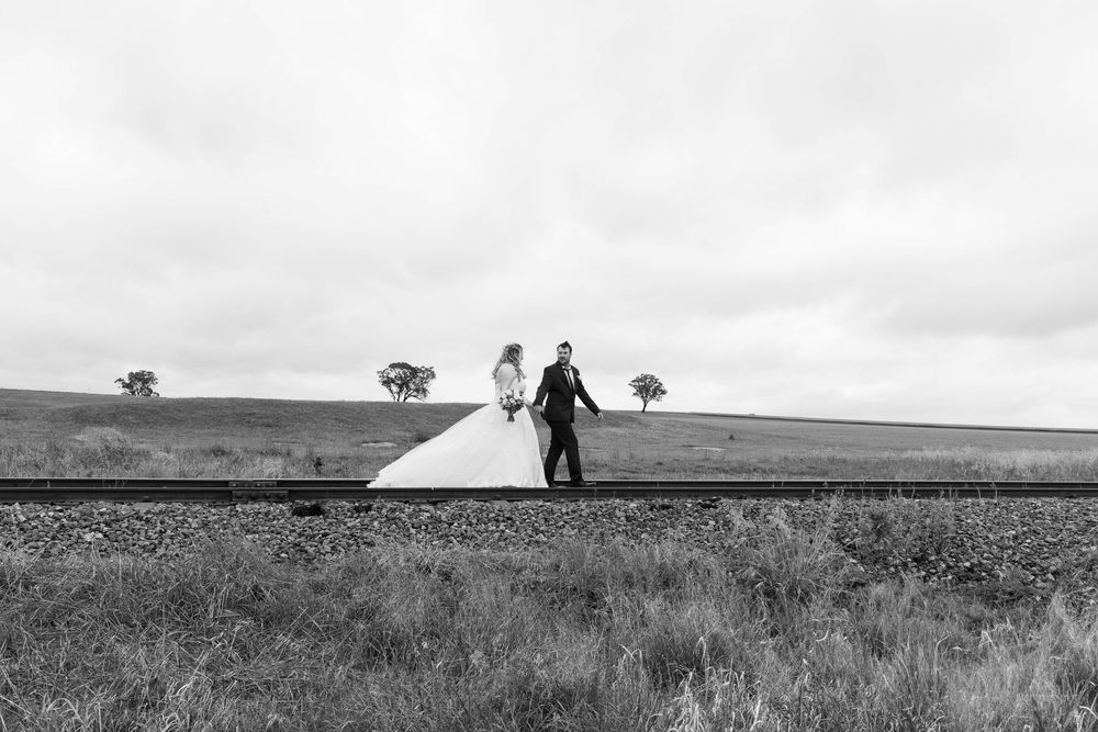 Wedding couple silhouettes walking through a vast open field under cloudy skies.