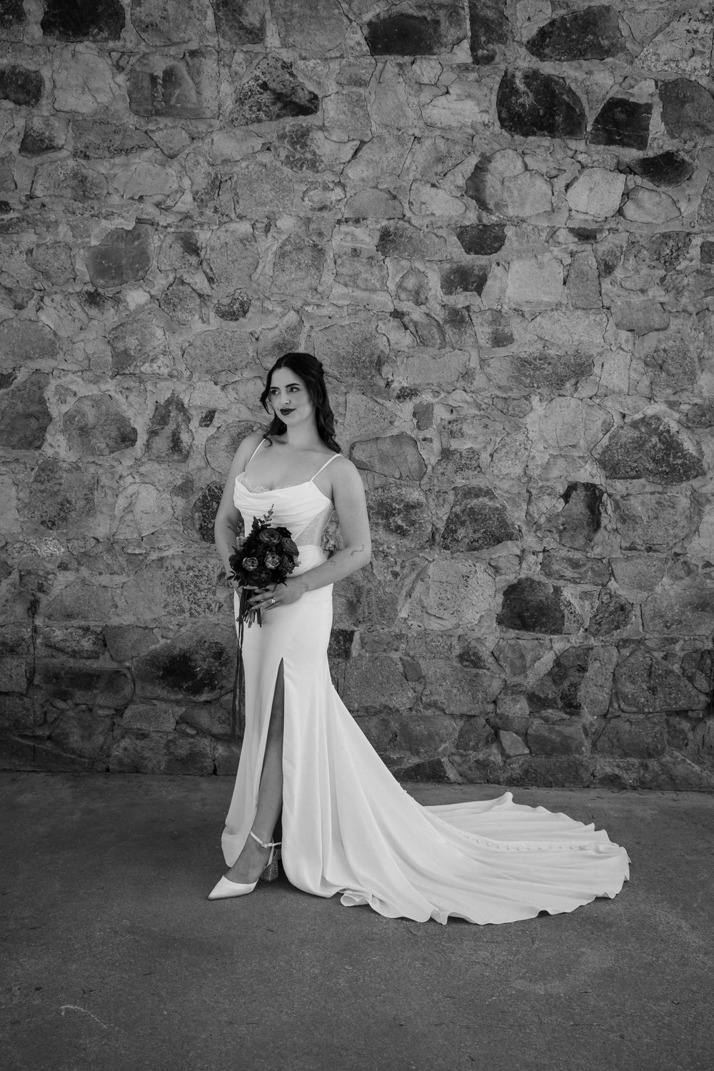 Elegant bridal portrait against stone wall showing flowing white wedding dress details.