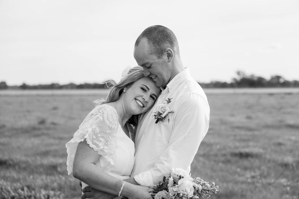 A romantic black and white wedding photo shows a tender moment between a couple embracing in an open field.