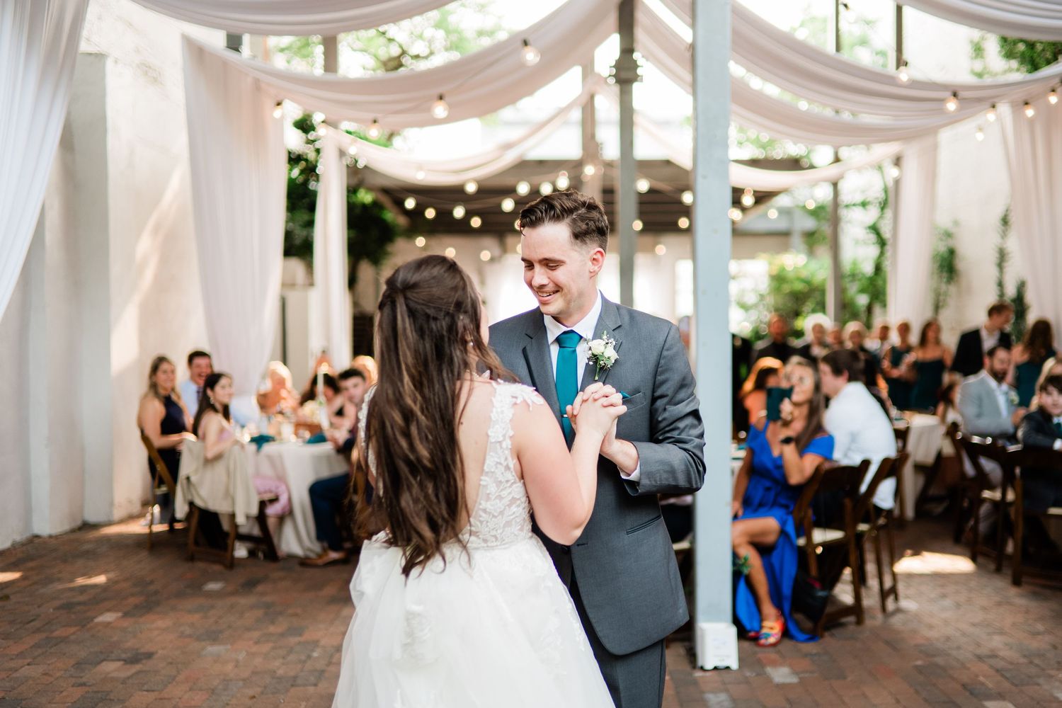 Guests gather at an elegant outdoor wedding reception under draped white fabric canopies with string lights.