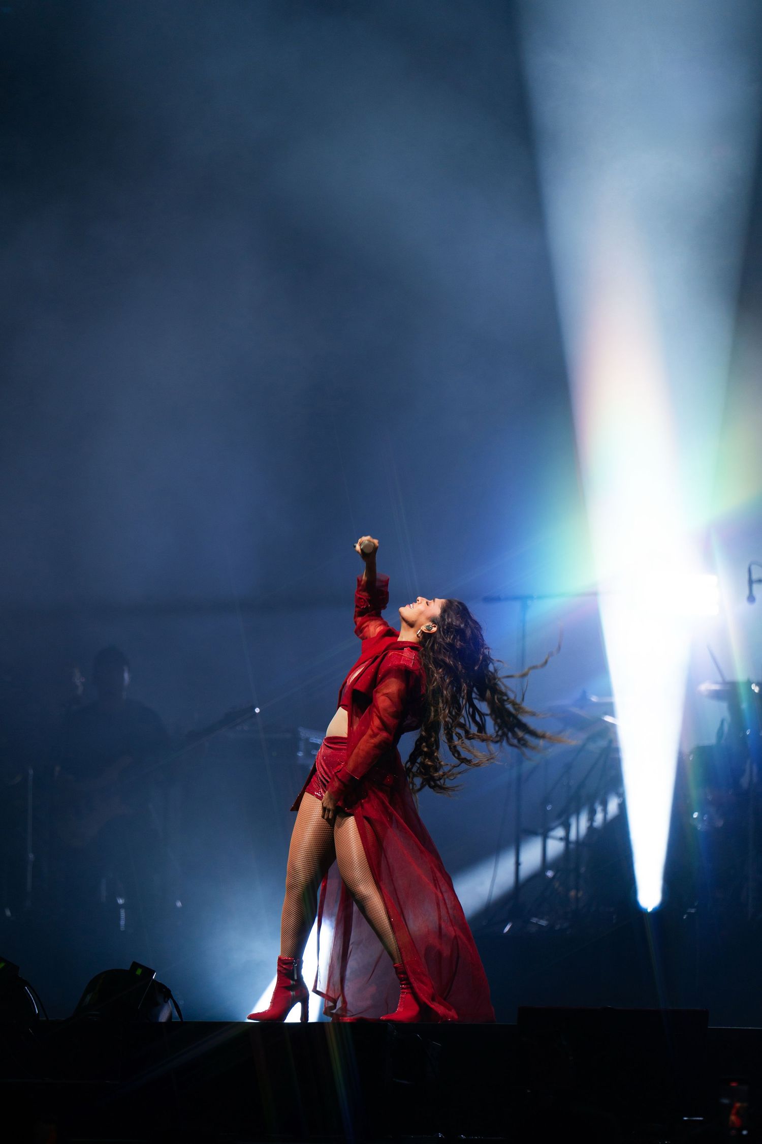 A performer in a striking red outfit dances dramatically on stage under dramatic blue and white spotlights.