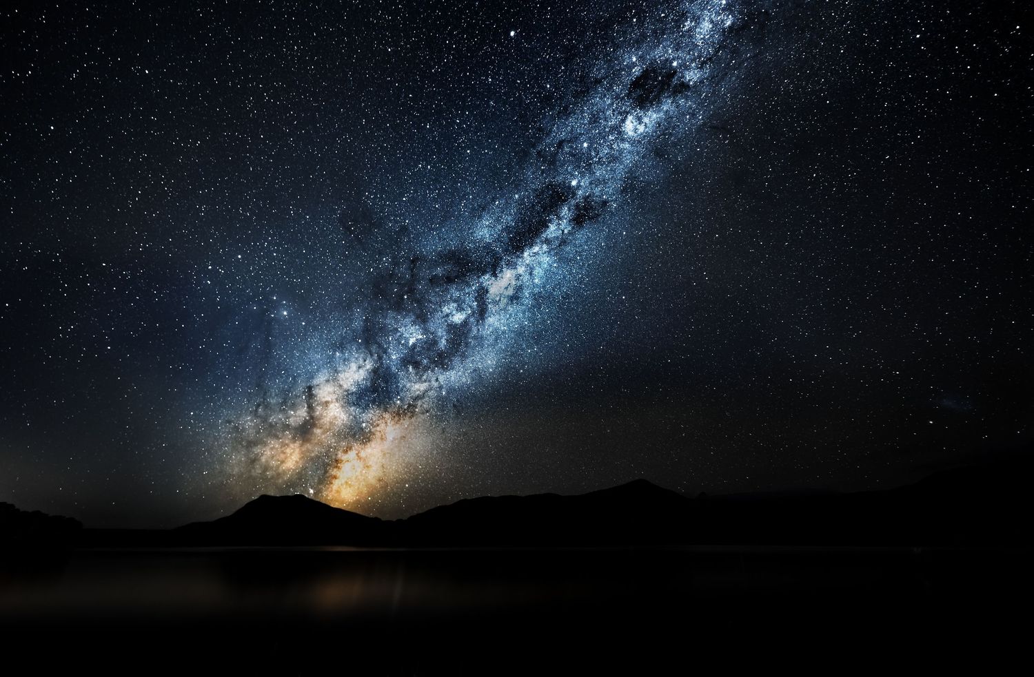 Milky Way galaxy core rising dramatically over dark mountain landscape at night.