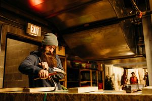 A restaurant worker in winter clothing pours hot beverages from a metal pot behind a dimly lit counter.