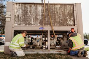 Workers in safety vests perform maintenance on a train car undercarriage during scheduled service repairs.