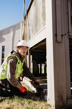 Construction workers in safety gear inspect the underside of an elevated building structure in daylight.