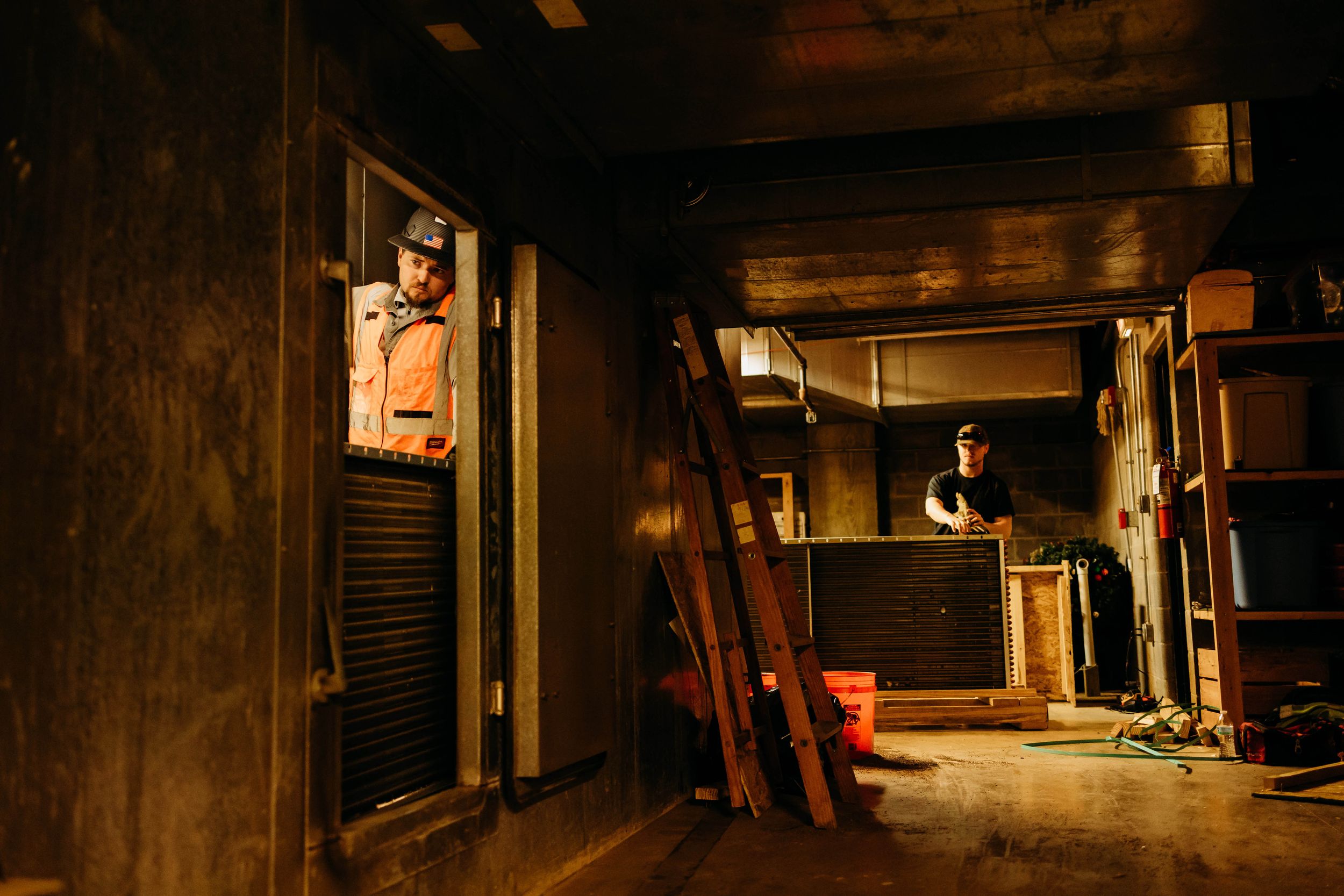 Dimly lit interior of a rustic wooden cabin or basement with tools and equipment stored along the walls.