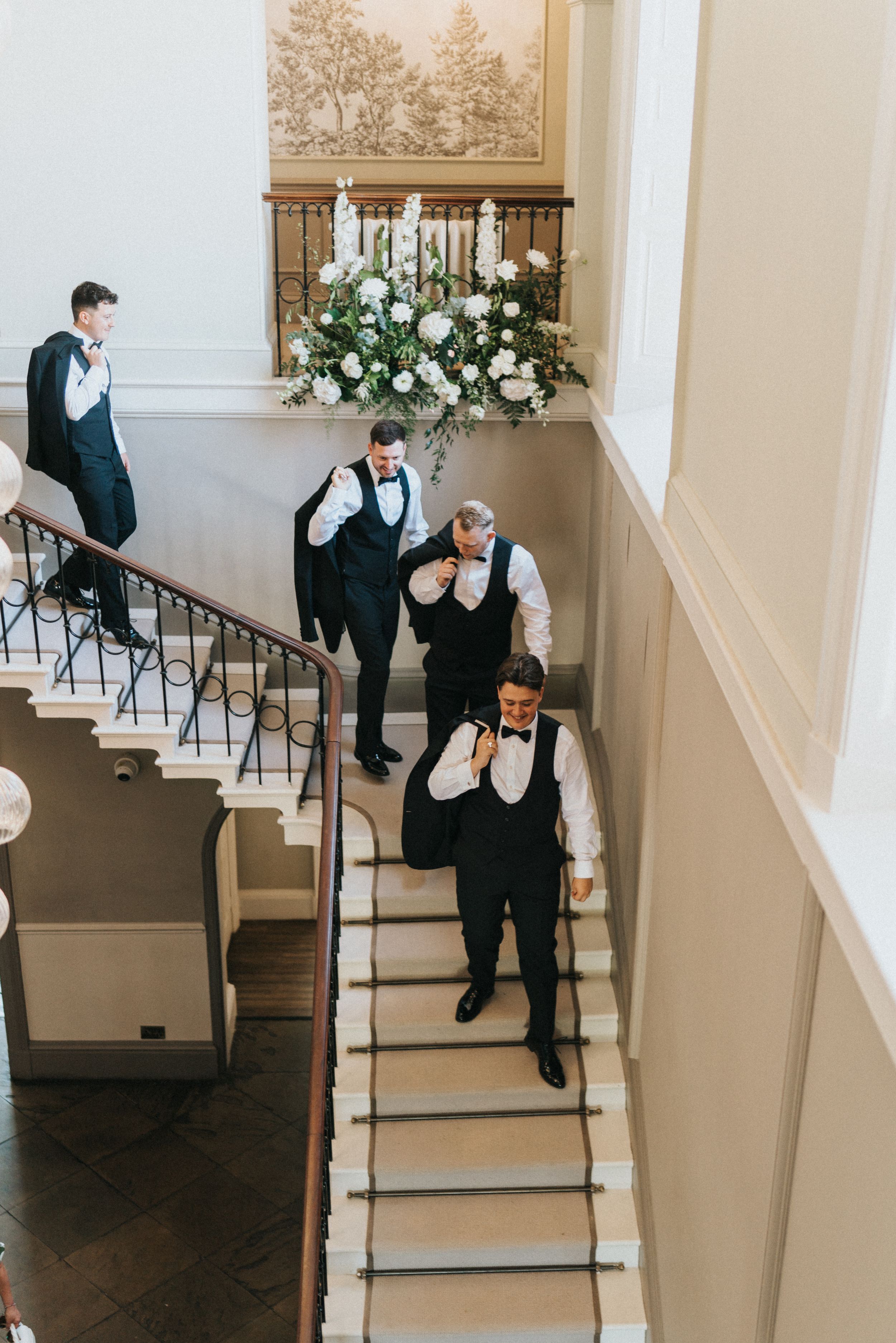 Groomsmen in black vests and bow ties pose on an elegant staircase at Saltmarshe Hall - taken by Grimsby photographer.