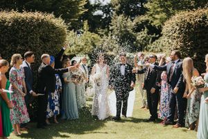 Wedding guests throw confetti over a newlywed couple during an outdoor summer garden celebration at Saltmarshe Hall.