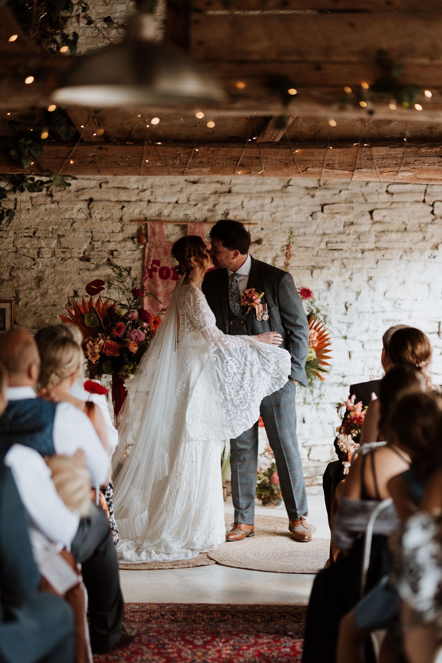 A sequence of black and white photos showing a couple's romantic first kiss during their wedding ceremony in a rustic brick venue.