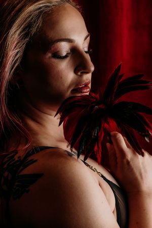 Multiple frames of a moody boudoir photo shoot featuring dark red lighting and black feathers against bare shoulders. Boudoir Photography Mi