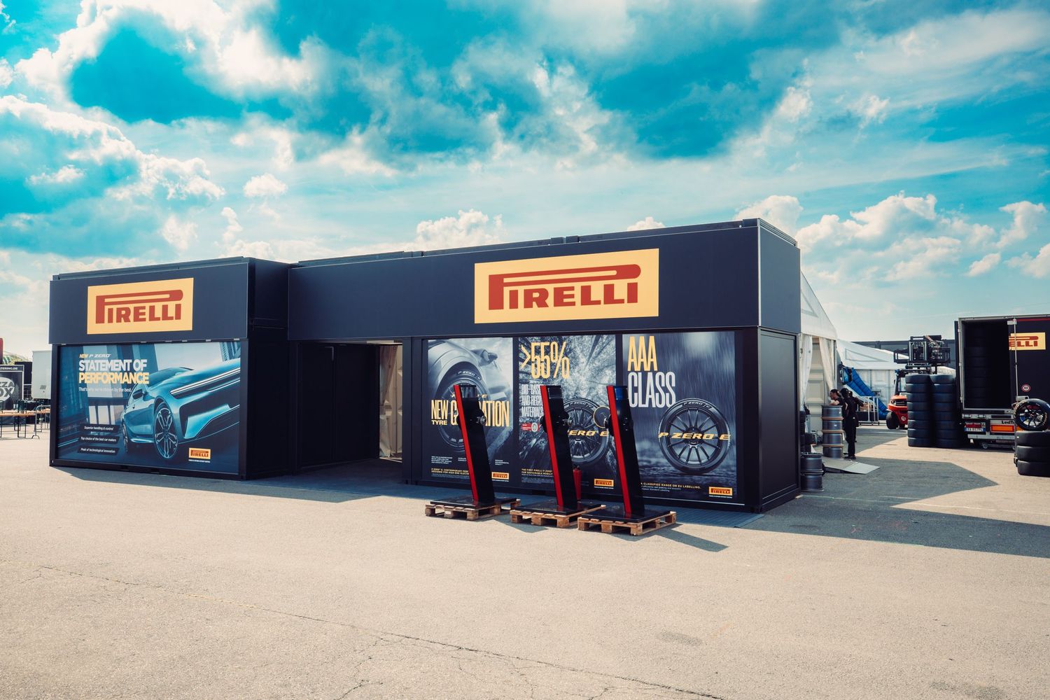 Car service facility exterior with Pirelli branding under bright blue sky with white puffy clouds.