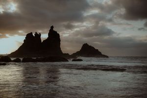 Dramatic rock formations rise from the ocean against a moody sunset sky with dark storm clouds. Playa de Benijo. Love Story in Tenerife.