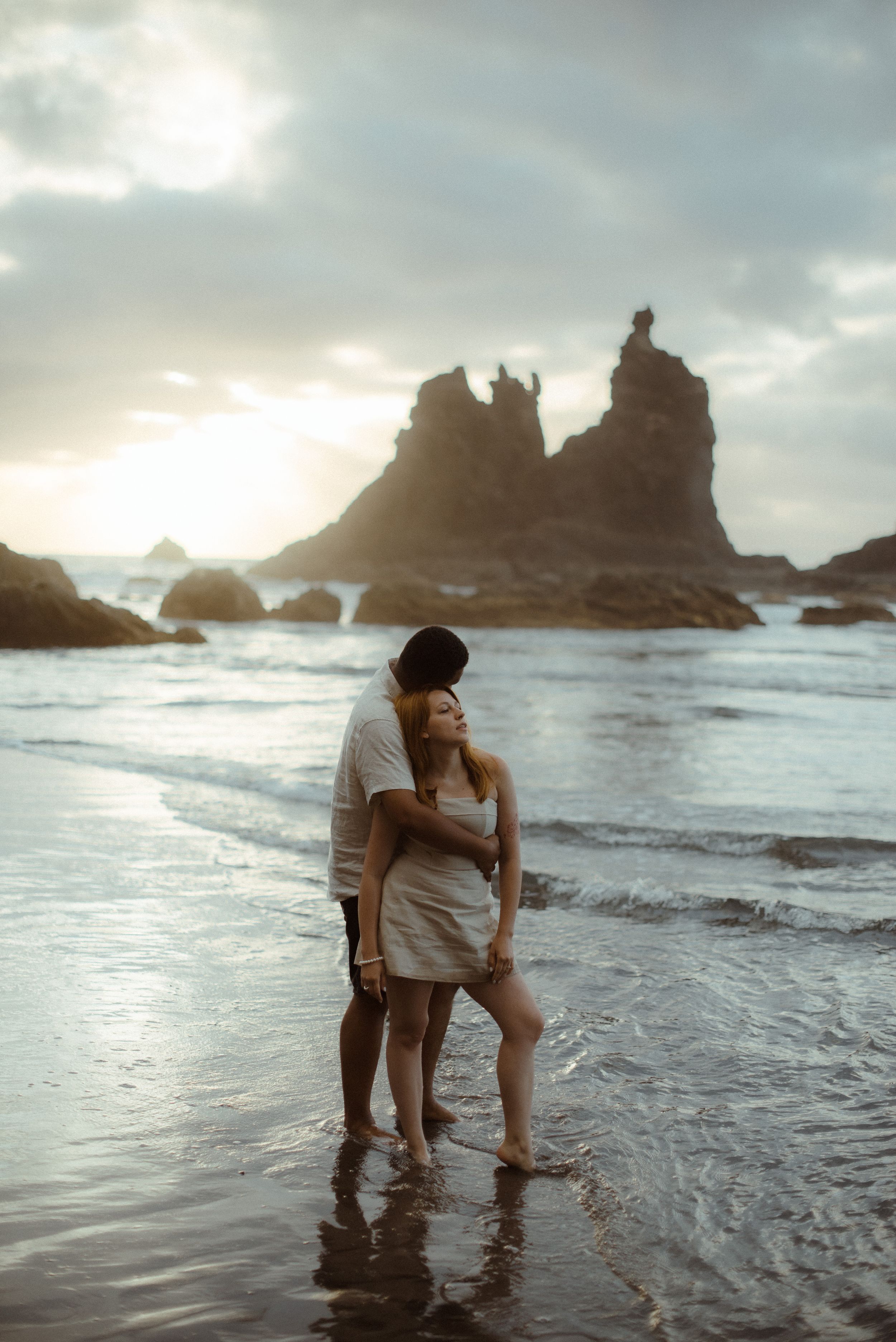 A couple standing in shallow ocean water at sunset with dramatic rock formations of Playa de Benijo. Love Story in Tenerife.