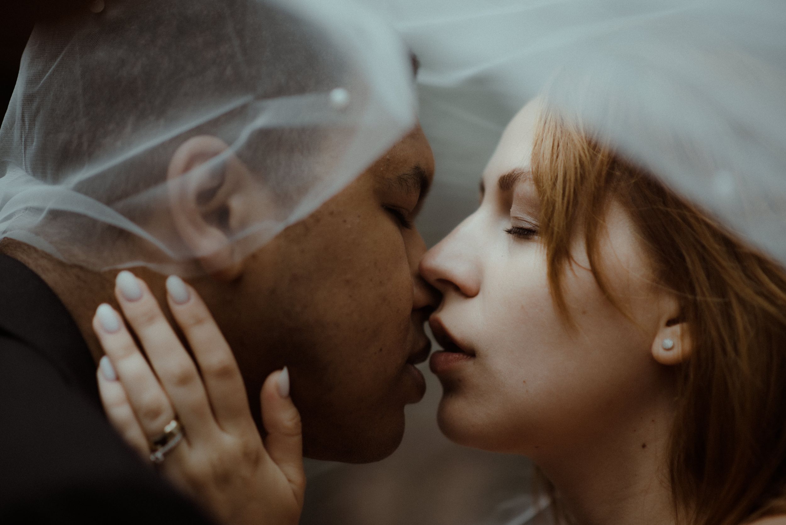 An intimate moment between newlyweds under a sheer veil during their wedding photoshoot.
