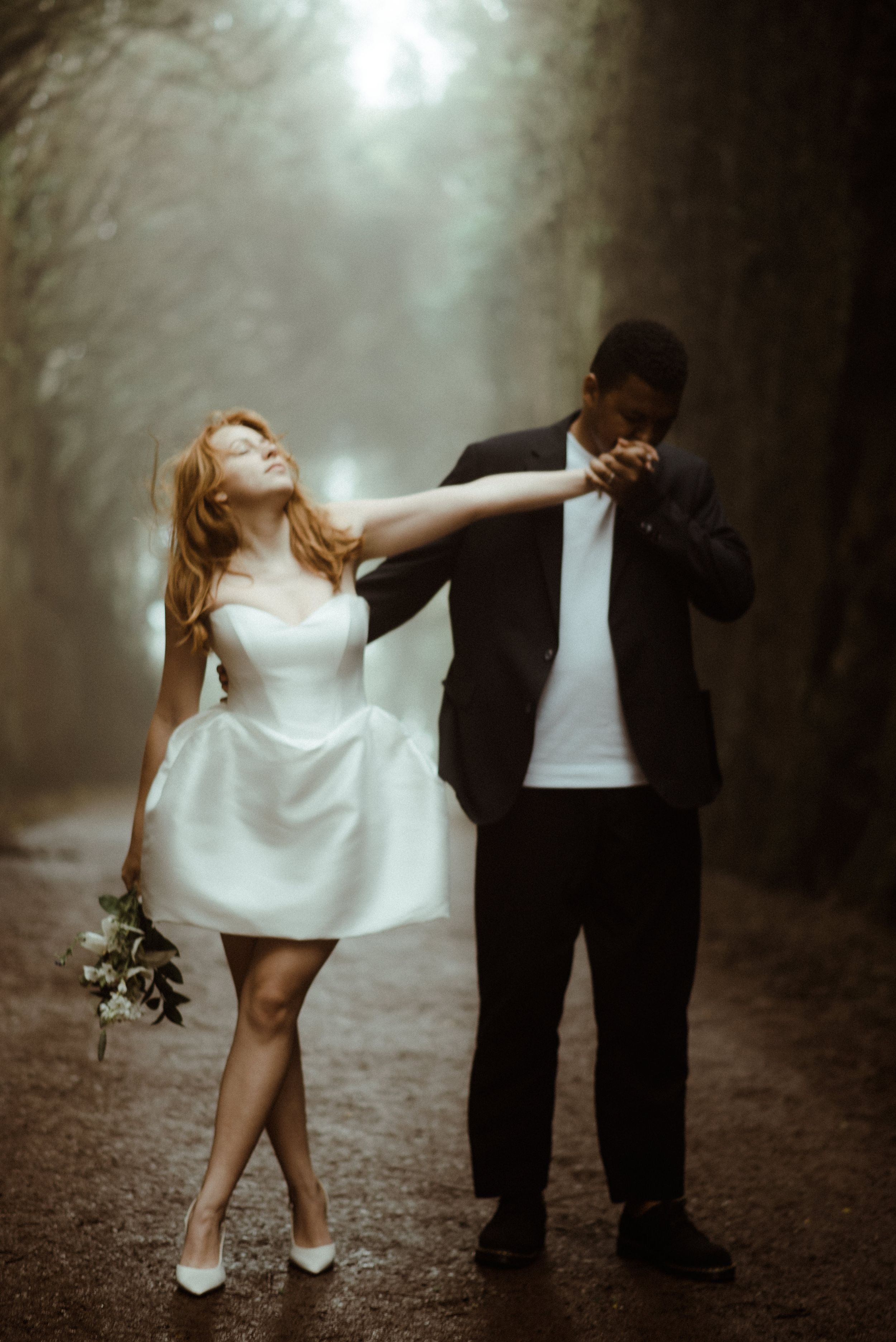 An artistic wedding photo of a couple in a misty forest pathway with dramatic lighting.