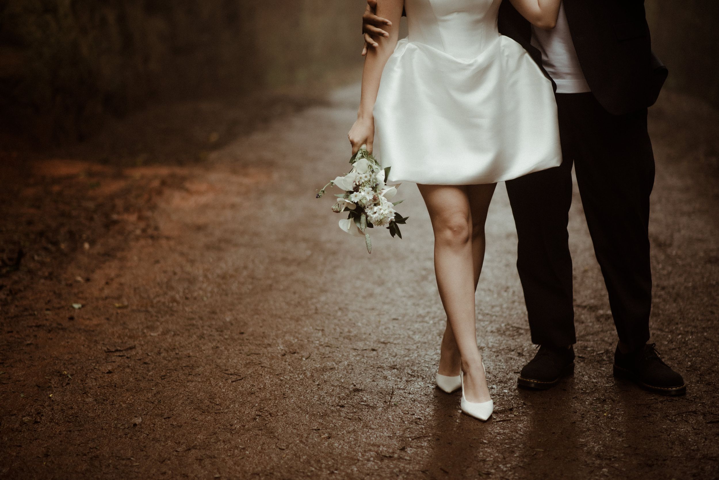 Close-up of wedding couple's legs and dress on a moody forest path.