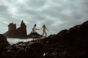 Silhouetted figures walk along rocky coastal cliffs under a dramatic cloudy sky. Playa de Benijo. Love Story in Tenerife.