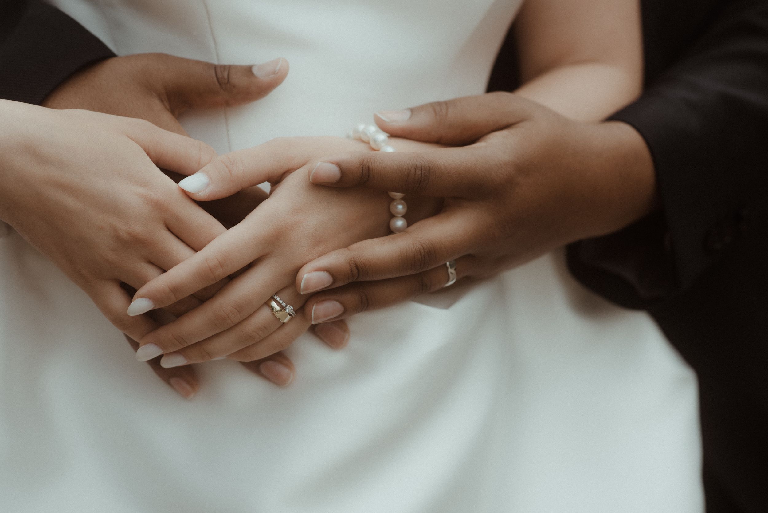 Close-up shot of hands with wedding rings resting on white fabric showing engagement and wedding bands.