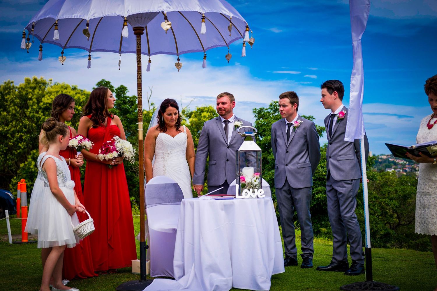 Outdoor wedding ceremony under purple tent with guests seated on lawn.
