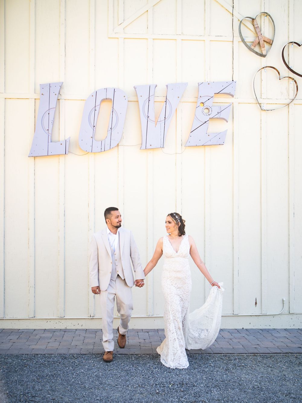 Couple poses beneath large white 'LOVE' letters on a light wall with decorative hearts.