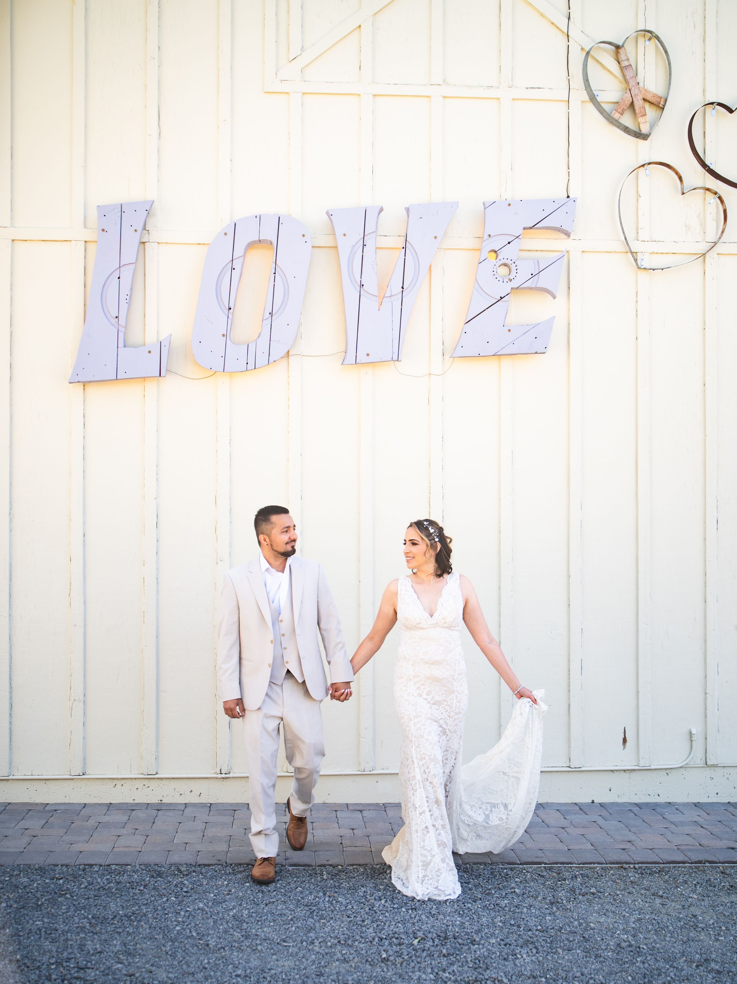 Couple poses beneath large white 'LOVE' letters on a light wall with decorative hearts.
