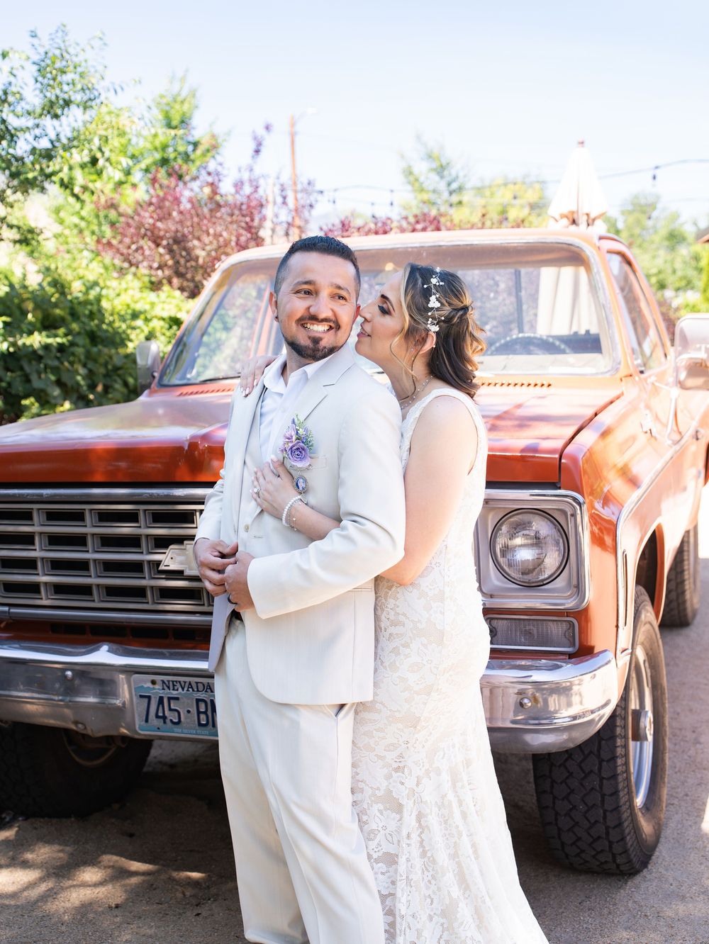 Romantic wedding couple shares tender moments in front of vintage orange truck on sunny outdoor photo shoot.