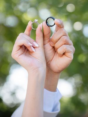 Hands holding two wedding rings against a blurred green bokeh background in natural lighting.