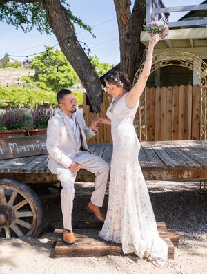 A couple celebrates their wedding day on a rustic wooden wagon in front of a gazebo on a sunny afternoon.