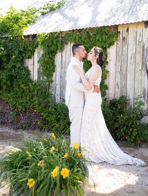 A romantic couple in white attire embracing by a rustic fence with yellow daylilies blooming in the garden.