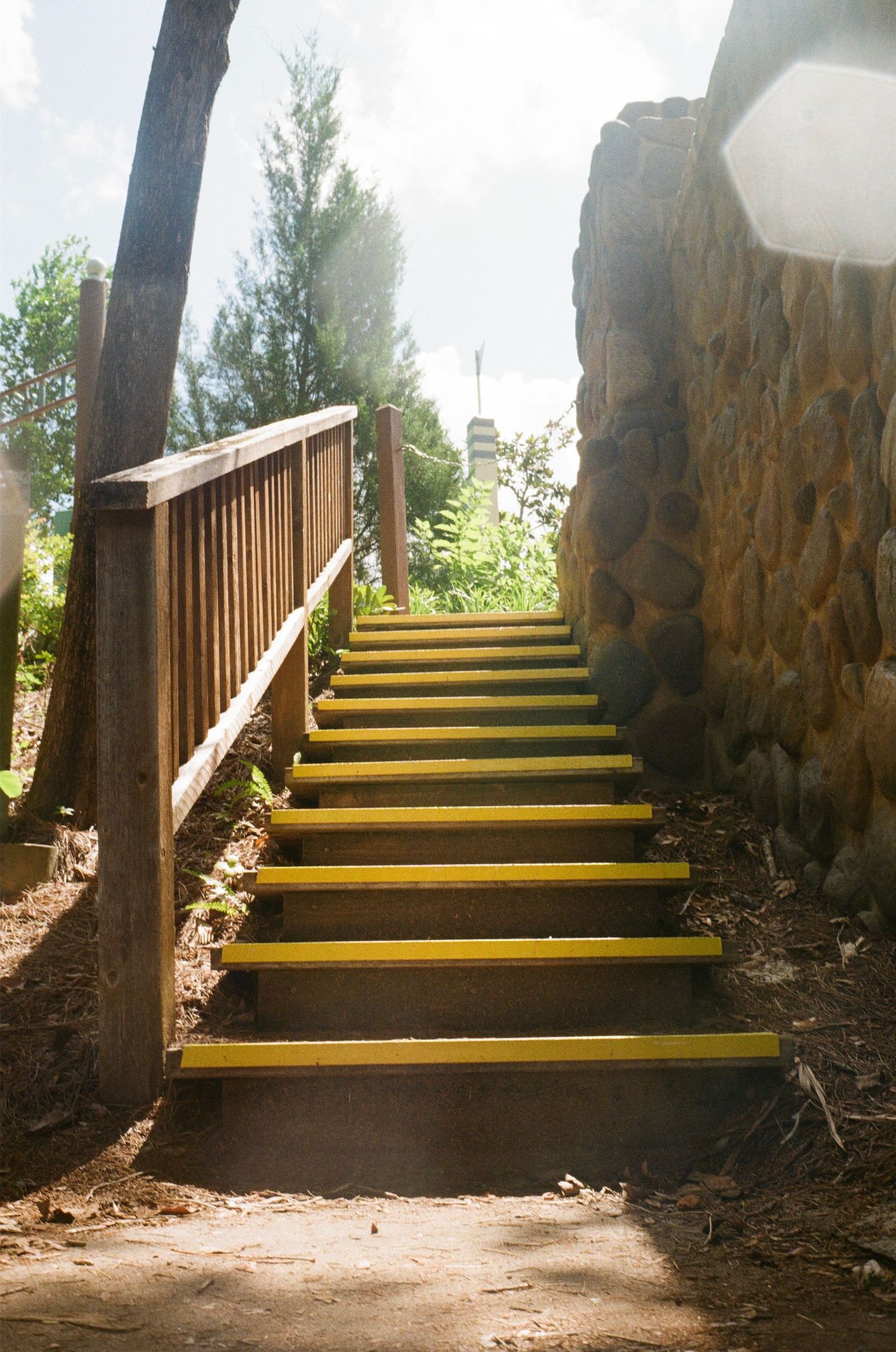 Artistic composition of stone archway leading up wooden steps with yellow edges illuminated by natural light.