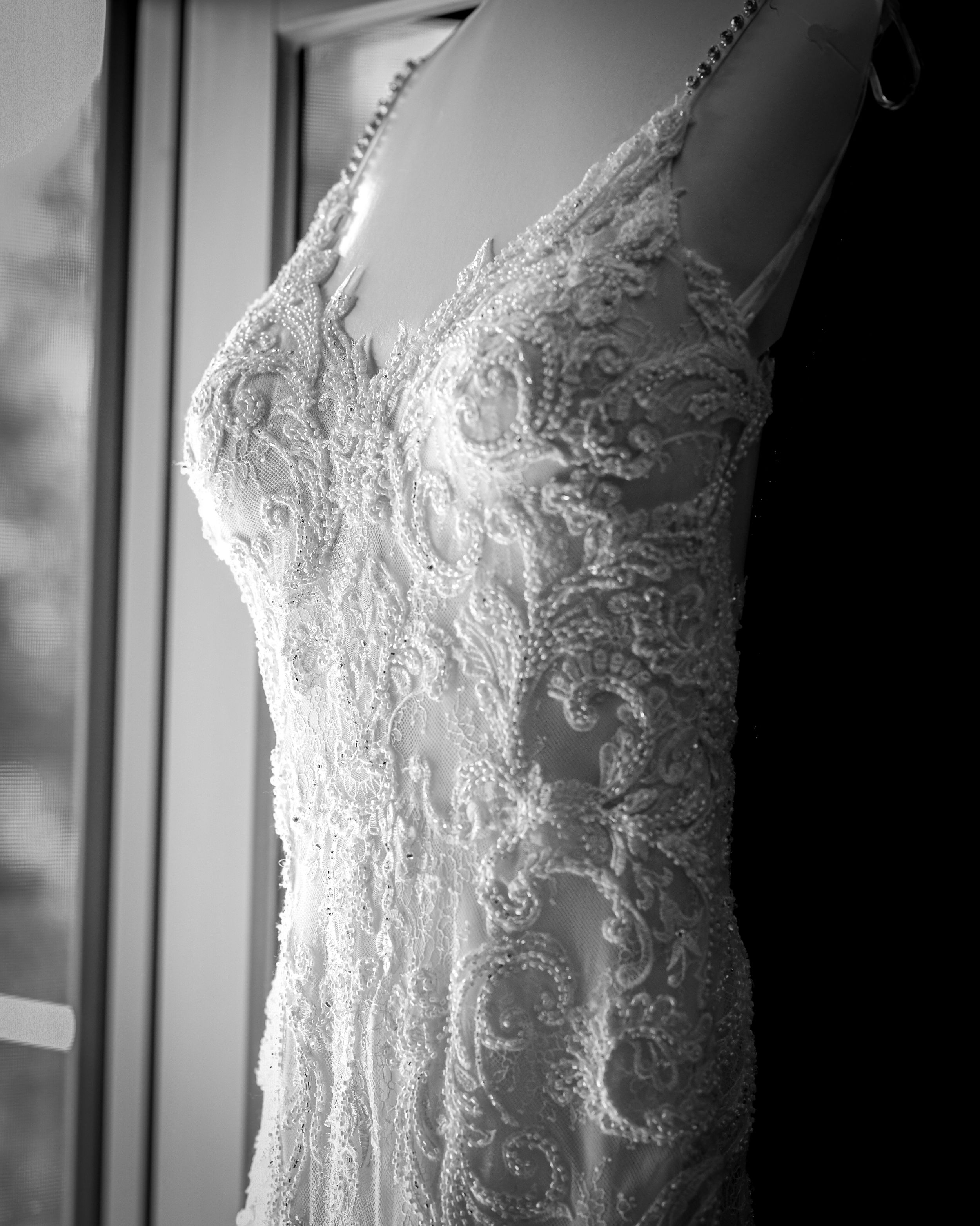 Black and white detail shot of a delicate lace wedding dress hanging.