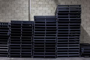 Black plastic pallets stacked neatly against a white brick wall in a warehouse setting.