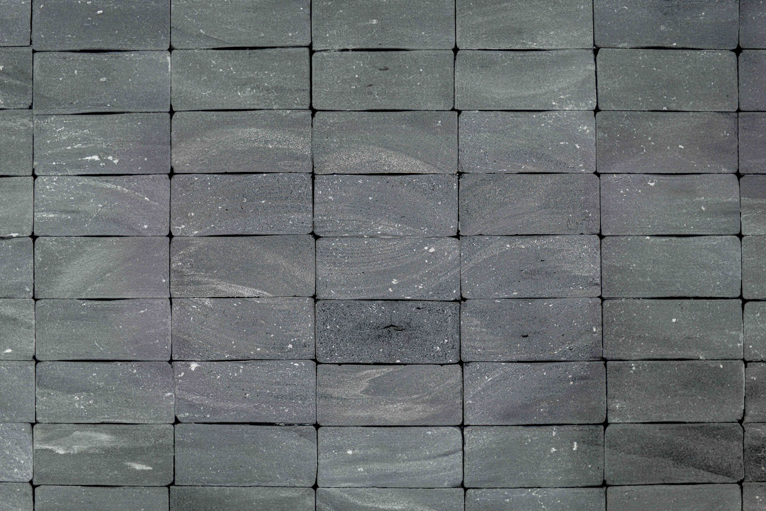 Close-up pattern of gray rectangular stone tiles arranged in uniform rows on a textured wall surface.