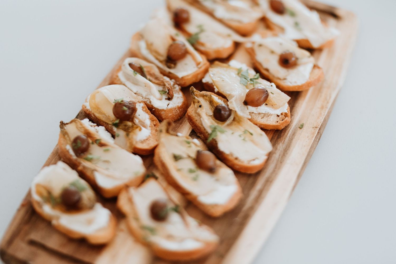 Small toasted bread appetizers topped with cream cheese, salmon, and capers arranged in rows on a wooden surface.