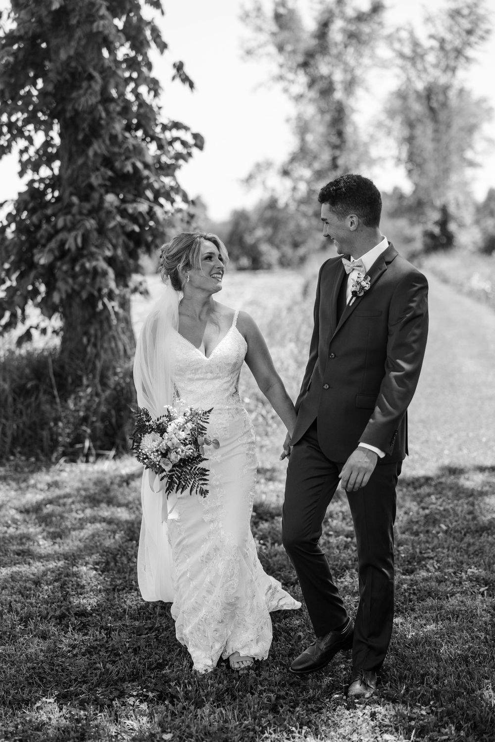 A black and white wedding photo captures a couple on a garden path, with the bride in white holding a bouquet.