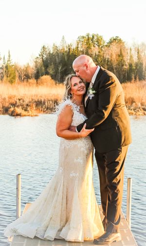 A romantic wedding couple embraces at sunset by a lake with golden fall foliage in the background.
